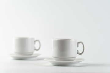 Two white empty cups and saucers on a white background. Selective focus.