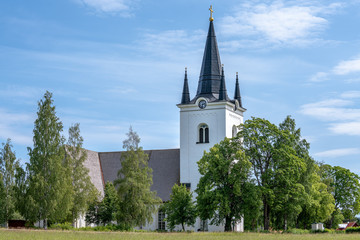 The beautiful white church in Svardsjo in Sweden surrounded by lush green trees