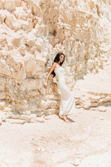 Elegant girl in a white dress rests on a rock