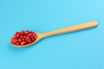 Red Pomegranate seed wooden spoon blue paper background