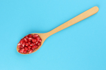 Red Pomegranate seed wooden spoon blue paper background