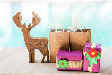 Christmas concept, Wood reindeer with blurred gift and gift in brown shopping bag over blurred blue water background, Christmas gift