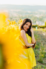 Beautiful girl in a yellow dress standing in a field of sunflowers