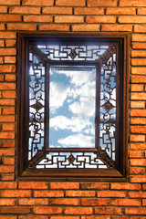 Wooden decorative window in a brick wall. A view of a blue summer sky through a window in the wall.