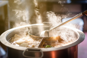 Cooking person in the restaurant is cooking while using the dipper in a large soup pot. And the...