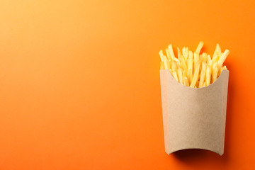Slices of hot french fries in box on orange background, space for text. Top view