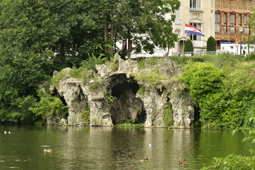 Fototapeta na wymiar La fausse grotte en rocaille entourée de végétation luxuriante au lac du square Marie-Louise à Bruxelles