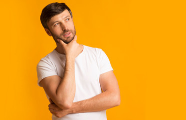 Pensive middle-aged guy standing touching chin thinking over yellow background