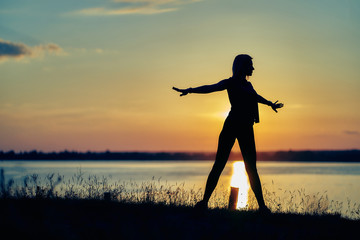 silhouette of a young woman at sunset. gymnastics, yoga, exercises, healthy lifestyle.