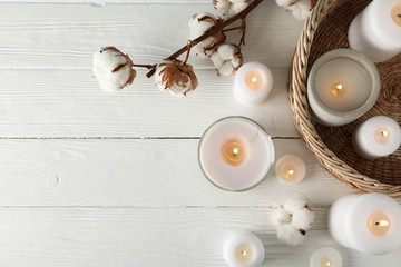 Burning candles, basket and cotton on white wooden background, top view