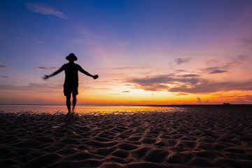 Fototapeta premium Silhouette man on the beach, at sunset. Happy lifestyle in holiday. Freedom life. colorful sky and cloudy view. For web banner