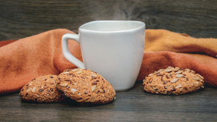 White mug with hot tea and oatmeal cookies with seeds on wooden background_