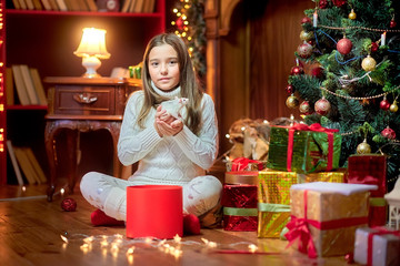 Fototapeta na wymiar Cute little girl sits on the floor near the Christmas tree holds in her arms and strokes a funny white rat on a background of bright holiday lights. Symbol of 2020. Pets