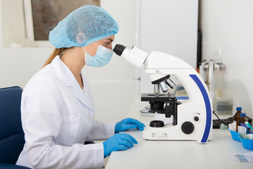 Naklejka na ściany i meble Young woman in medical clothes working with microscope