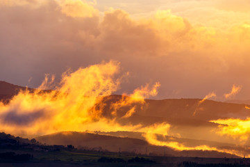 Low clouds in backlight over a rolling landscape at sunset