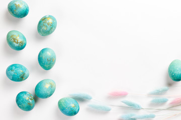 Happy easter card. Stylish minimalistic composition of turquoise with gold easter eggs on a white background. Delicate spring flowers. Flat lay, top view, copy space.