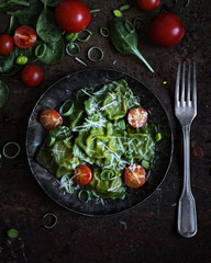 food photography of bright green spinach ravioli with cherry tomatoes and parmesan in a dark metal plate on an old rusty background with vegetables top view