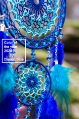 Dreamcatcher made of feathers, leather, beads, and ropes in classic blue trendy Color of the year 2020.