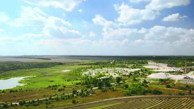 Aerial shot of a white clay processing plant of kaolin ore. Beautiful steppe green nature, blue sky with clouds, and pipes that smoke emissions into the clean air atmosphere. Environmental pollution.