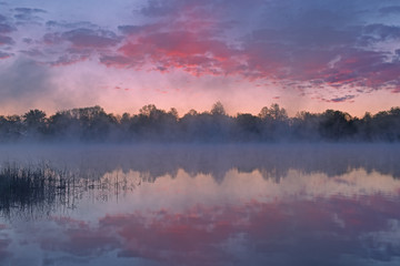 Foggy landscape at dawn of Whitford Lake with reflections in calm water, Fort Custer State Park, Michigan, USA