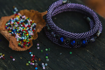 Beautiful, shiny, color bracelet with large beadwork beads. On a special stand for jewelry. Beads are scattered on a wooden table.