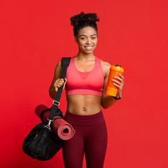 Portrait of happy fitness girl with sporty bag, mat, shaker
