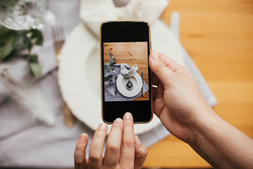 Taking photo of stylish Easter flat lay table setting with egg in easter bunny napkin on phone. Modern Easter table decorations workshop. Photo for social media, instagram