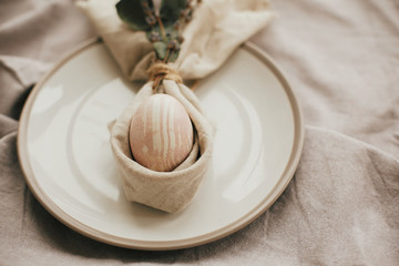 Stylish Easter brunch table setting with egg in easter bunny napkin. Modern natural dyed pink egg on napkin with bunny ears, lavender flowers on plate. Easter table decorations