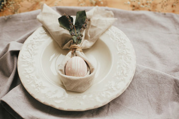 Stylish Easter brunch table setting with egg in easter bunny napkin. Modern natural dyed pink egg on napkin with bunny ears, lavender flowers on vintage plate. Easter table decorations