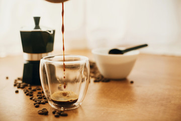 Pouring coffee in glass cup on background of roasted coffee beans, grounded coffee, geyser coffee maker on wooden table. Alternative Coffee brewing concept. Process of making espresso