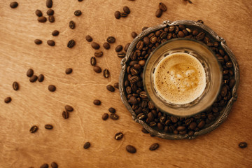 Hot espresso with foam in glass cup on vintage plate with aromatic roasted coffee beans on wooden table. Flat lay with copy space. Alternative Coffee brewing concept.