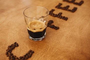 Coffee text word made of aromatic roasted coffee beans and glass cup of hot espresso on wooden table. Making Alternative coffee concept. International coffee day