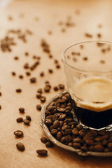 Hot espresso with foam in glass cup on vintage plate with aromatic roasted coffee beans on wooden table. Copy space. Alternative Coffee brewing concept.