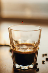Coffee drops close up in warm light while pouring hot espresso in glass cup on background of roasted coffee beans on wooden table. Alternative Coffee brewing concept. Copy space