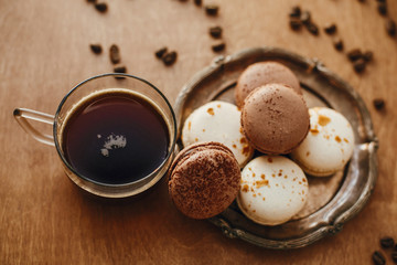 Coffee in glass cup and delicious macaroon cookies on vintage plate on wooden table with roasted coffee beans. Morning coffee and breakfast. Espresso with sweets
