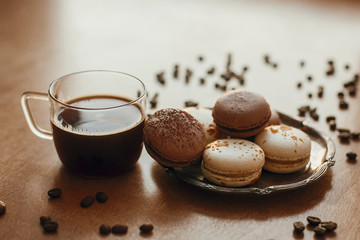 Coffee in glass cup and delicious macaroon cookies on vintage plate on wooden table with roasted coffee beans. Morning coffee and breakfast. Espresso with sweets