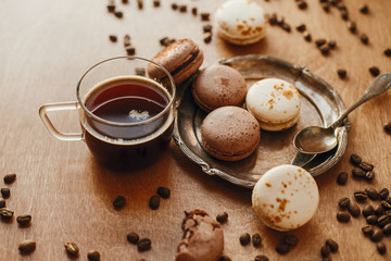 Coffee in glass cup and delicious macaroon cookies on vintage plate on wooden table with roasted coffee beans. Morning coffee and breakfast. Espresso with sweets