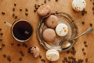 Coffee in glass cup and delicious macaroon cookies on vintage plate on wooden table with roasted coffee beans. Flat lay. Morning coffee and breakfast. Espresso with sweets