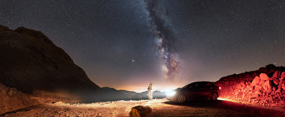 Panorama of milky way and two people standing near car and looking up to the sky - 308755667