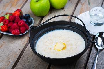 Traditional breakfast milk porridge with butter and berries on a wooden table.