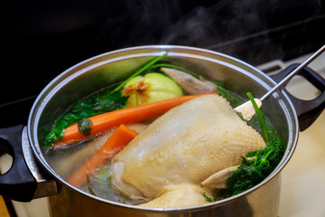 Boiling chicken broth with vegetables in steel pot on gas stove top.