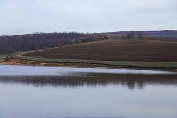 road over a cliff of a lake along a plow field