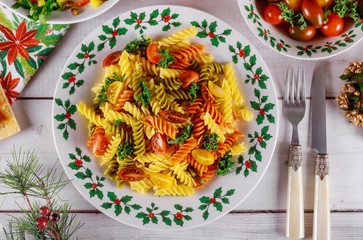 Rotini pasta and cherry tomato with green salad on christmas table.
