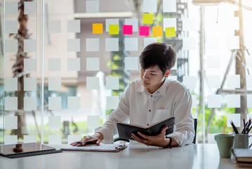 Portrait of young asian businessman sitting and thinking and analyzing documents at his desk in the office.
