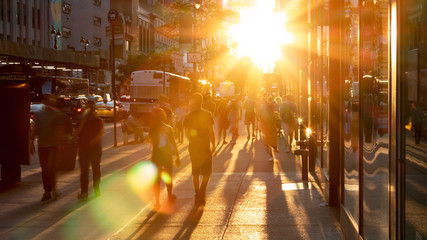 Sunlight shines on the diverse crowds of people walking down the busy sidewalk on 34th Street...