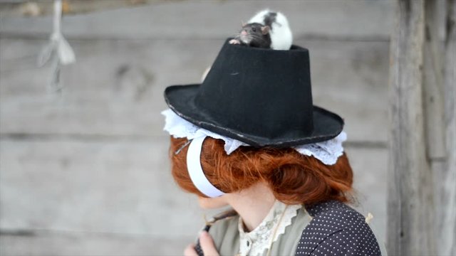 Manual domestic rat sits in a hat at a cheerful red-haired girl