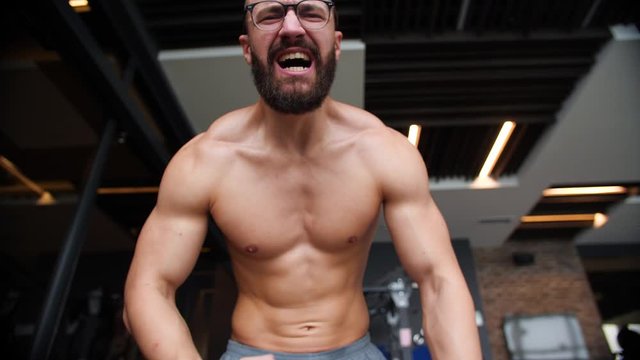 Ripped Shirtless Man with glasses screaming at the camera and flexing his muscles