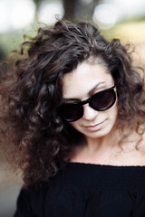 Fototapeta premium Portrait of a curly young brunette woman in sunglasses on a sunny summer day.