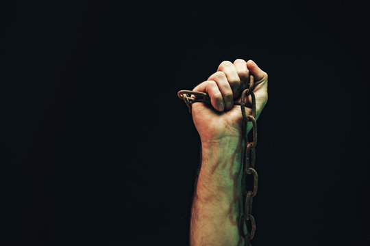 Human Hand Are Chained In Chains Isolated On Black Background.