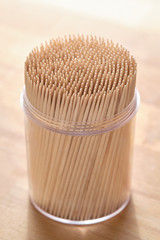 Bright still life with a transparent plastic mug full of new wooden toothpicks standing on a wooden table